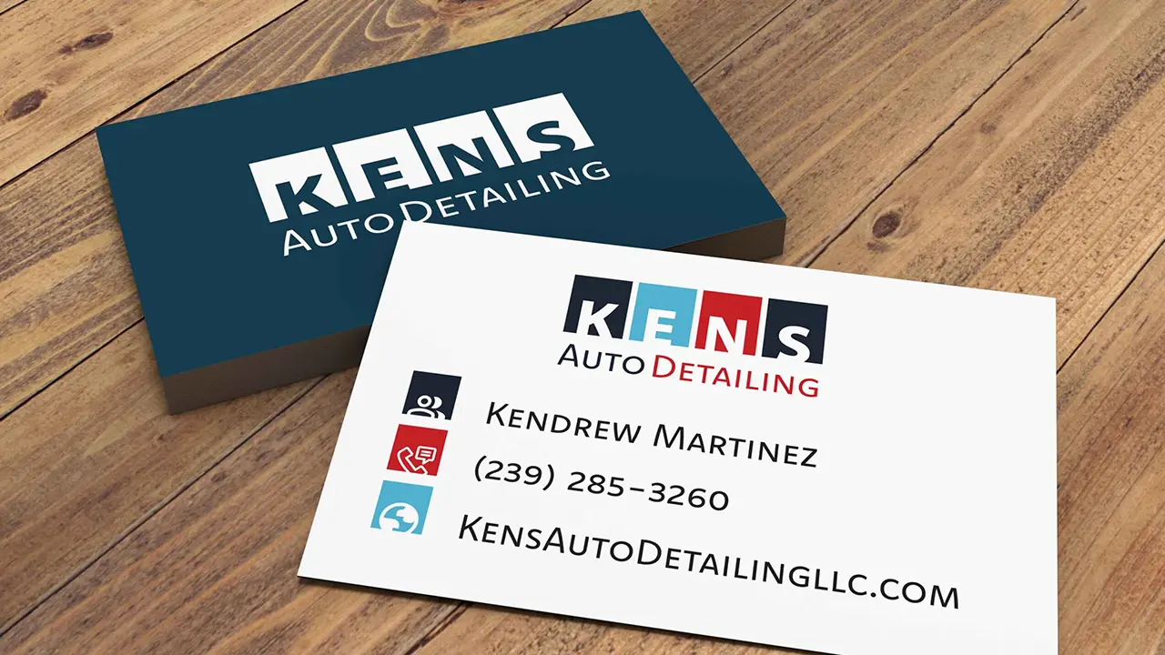 Business cards for Kens Auto Detailing displayed on a wooden table.